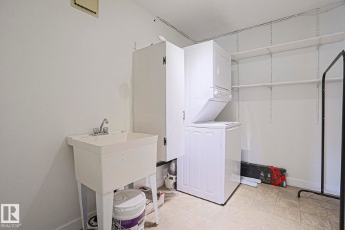 Dedicated laundry area featuring a utility sink with dual-handle faucet, a stacked washer and dryer, and adjustable wall shelving - 205 14903 92 Avenue Nw, Edmonton, AB 