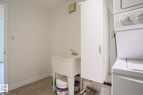 Laundry area featuring a utility sink, wall-mounted cabinetry, and stacked washer and dryer - 205 14903 92 Avenue Nw, Edmonton, AB 