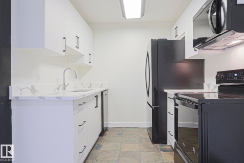 Compact kitchen featuring white cabinetry with dark pulls, a gooseneck faucet, and stone-look countertops - 205 14903 92 Avenue Nw, Edmonton, AB 