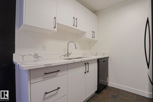 Contemporary kitchen featuring white cabinetry with matte black hardware, a stainless steel sink with a high-arc faucet, and a dishwasher - 205 14903 92 Avenue Nw, Edmonton, AB 