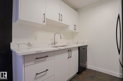 Contemporary kitchen featuring white cabinetry with matte black hardware, a stainless steel sink with a high-arc faucet, and a dishwasher - 