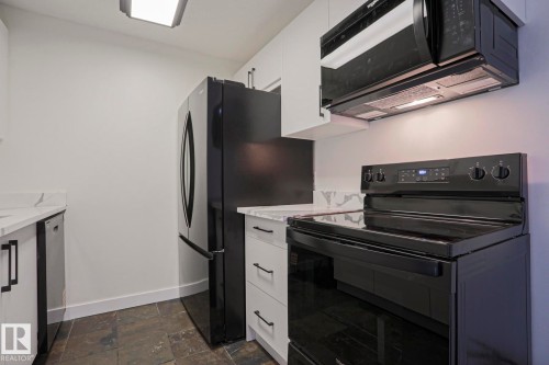 Modern kitchen featuring white cabinetry with matte black hardware, stone-finish countertops, and full-size black appliances including a refrigerator, range, and microwave - 205 14903 92 Avenue Nw, Edmonton, AB 