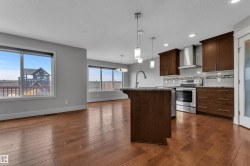 Open-concept kitchen and living area featuring dark wood-finish cabinetry, stainless steel appliances, a center island with pendant lighting, and wood-finish flooring - 