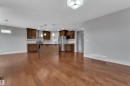 Open-concept kitchen and living area featuring wood-finish flooring, warm gray wall tones, dark wood cabinetry, a central island, and stainless steel appliances - 3363 13 Ave, Edmonton, AB 