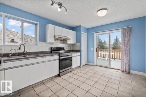 Kitchen with white cabinetry, stainless steel appliances, and a double basin sink with an arched faucet - 8103 154 Avenue, Edmonton, AB 