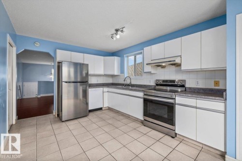 Kitchen featuring white cabinetry, stainless steel appliances, speckled countertops, ceramic tile flooring, and a tile backsplash - 8103 154 Avenue, Edmonton, AB 