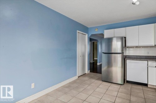 Kitchen area featuring square tile flooring, stainless steel refrigerator, white cabinetry, white dishwasher, and light blue wall paint - 8103 154 Avenue, Edmonton, AB 