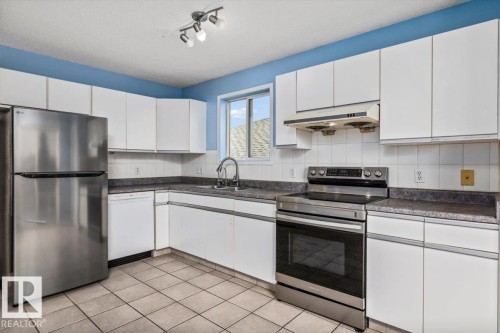 Kitchen featuring white cabinetry, tile flooring, and integrated stainless-steel appliances - 8103 154 Avenue, Edmonton, AB 