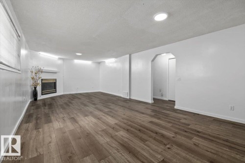 Spacious room featuring wood-finish flooring, a built-in fireplace with a mantel, recessed lighting, and a window with blinds - 8103 154 Avenue, Edmonton, AB 