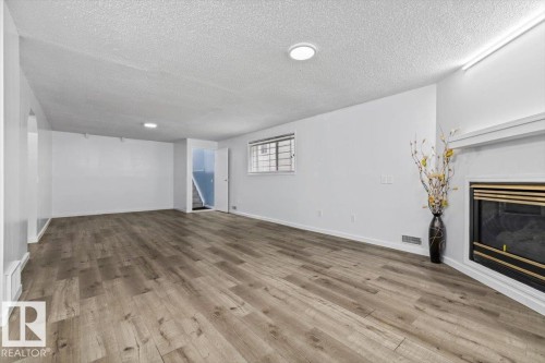 Spacious interior featuring wood-finish flooring, a corner fireplace with a white mantel, and a window with security bars - 8103 154 Avenue, Edmonton, AB 