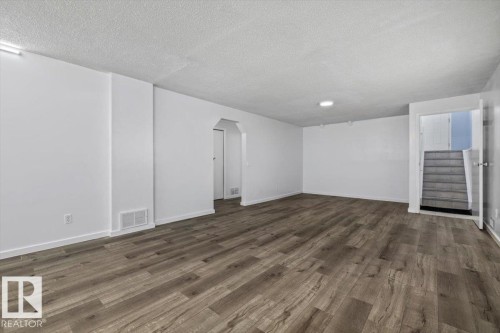 Spacious room featuring wood-finish flooring, white painted walls, white baseboards, a textured ceiling, and recessed lighting - 8103 154 Avenue, Edmonton, AB 
