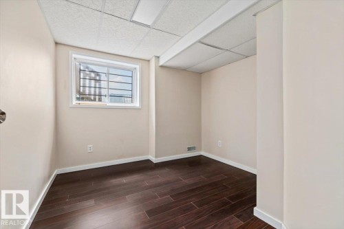 Room featuring dark wood-finish flooring, light-toned walls, and a drop ceiling with integrated lighting - 8103 154 Avenue, Edmonton, AB 