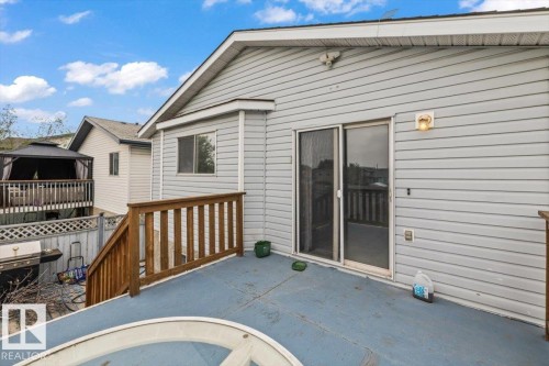 Rear exterior featuring a spacious upper deck with blue-painted flooring and wood railing, providing direct access via a glass sliding door - 8103 154 Avenue, Edmonton, AB 
