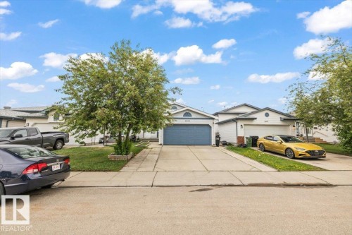 Front exterior featuring a light-colored facade, an attached two-car garage with a blue door, and a concrete driveway - 8103 154 Avenue, Edmonton, AB 