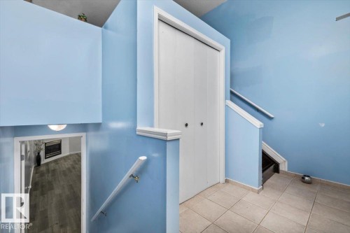 Interior landing featuring white bi-fold closet doors, tile flooring, and a white wall-mounted handrail - 8103 154 Avenue, Edmonton, AB 