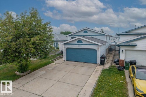 Residential property with an attached garage, featuring light-colored siding and a blue garage door - 8103 154 Avenue, Edmonton, AB 