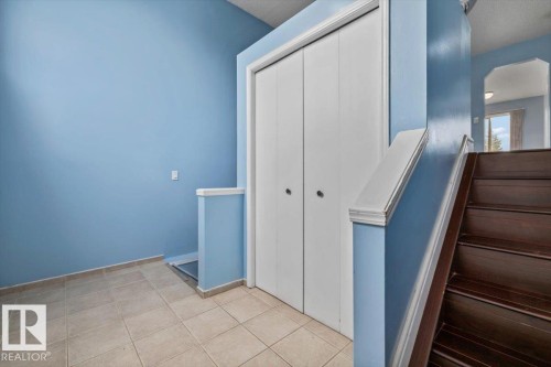 Foyer featuring large format tile flooring, a double-door closet, and dark wood-finish stairs with a coordinating banister - 8103 154 Avenue, Edmonton, AB 