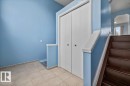 Foyer featuring large format tile flooring, a double-door closet, and dark wood-finish stairs with a coordinating banister - 8103 154 Avenue, Edmonton, AB 