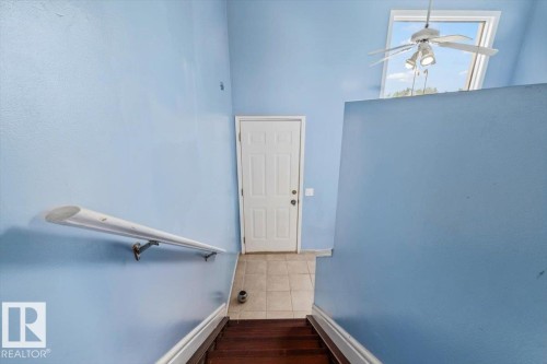 Stairwell featuring wood-finish treads and a neutral wall-mounted handrail leading to a tiled landing - 8103 154 Avenue, Edmonton, AB 