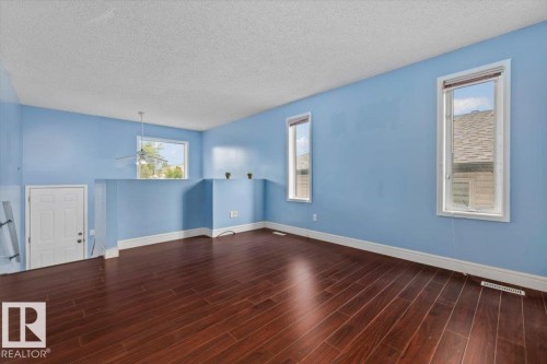 Spacious interior featuring rich wood-finish flooring, light blue walls, and a white ceiling - 8103 154 Avenue, Edmonton, AB 