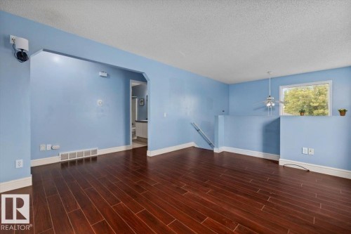 Spacious interior featuring rich wood-finish flooring, an arched doorway, and a ceiling fan with integrated lighting - 8103 154 Avenue, Edmonton, AB 