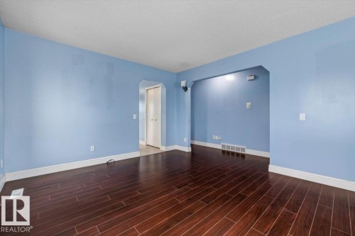 Spacious room featuring rich wood-finish flooring, light blue walls, white trim, and an arched doorway - 8103 154 Avenue, Edmonton, AB 