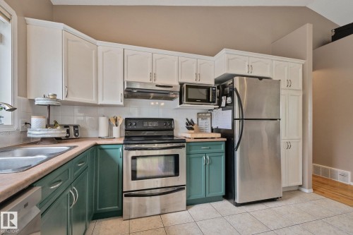 Kitchen featuring white upper cabinetry, teal lower cabinetry, stainless steel appliances, a tile backsplash, and light-toned countertops - 14 53122 Rge Road 14, Rural Parkland County, AB 