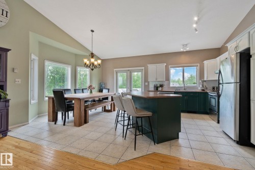 Open-concept kitchen and dining area featuring a central island with seating, a mix of white and deep green cabinetry, stainless steel appliances, and tile flooring - 14 53122 Rge Road 14, Rural Parkland County, AB 