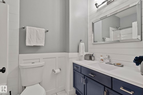 Bathroom featuring a dark blue vanity with a white countertop and integrated sink, a rectangular framed mirror, and a white toilet - 14 53122 Rge Road 14, Rural Parkland County, AB 