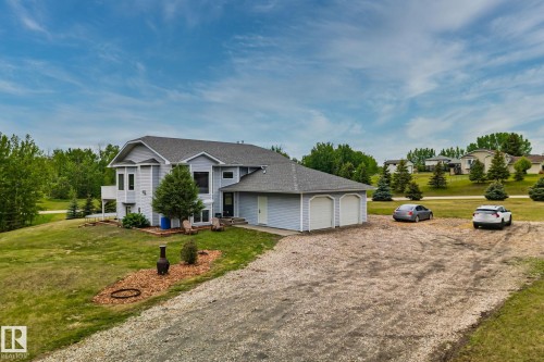 Light blue siding residence with a two-car garage, gravel driveway, and a sloped lawn featuring mature trees - 14 53122 Rge Road 14, Rural Parkland County, AB 