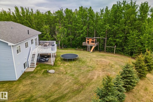 Spacious backyard featuring an elevated deck with white railings, a ground-level patio, and mature trees bordering the property - 14 53122 Rge Road 14, Rural Parkland County, AB 