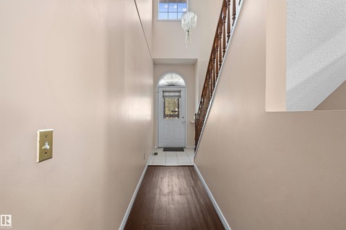 Entryway featuring wood-finish flooring, a white arch-top door with glass insert, and a double-height ceiling - 5 20 Deerbourne Drive, St. Albert, AB 