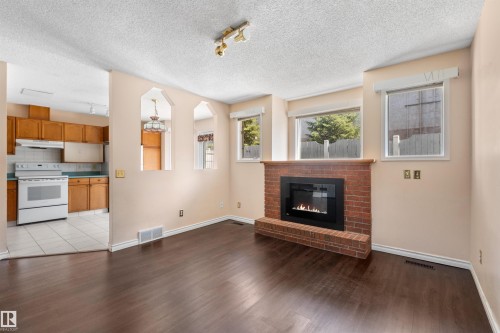 Spacious living area featuring rich wood-finish flooring, a brick-front fireplace, and multiple windows - 5 20 Deerbourne Drive, St. Albert, AB 