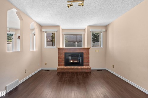 Living area featuring a brick fireplace with a wood mantle, an integrated fireplace insert, dark wood-finish flooring, and recessed wall cutouts - 5 20 Deerbourne Drive, St. Albert, AB 