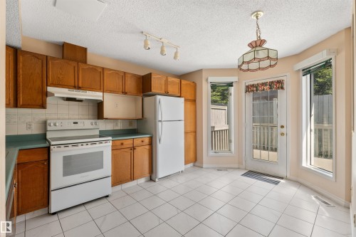 Kitchen featuring wood cabinetry, white appliances, white tile flooring, and a glass-paneled door with surrounding windows - 5 20 Deerbourne Drive, St. Albert, AB 