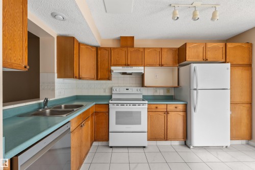 Kitchen featuring wood-finish cabinetry, white tile flooring, white tile backsplash, and a double basin stainless steel sink - 5 20 Deerbourne Drive, St. Albert, AB 