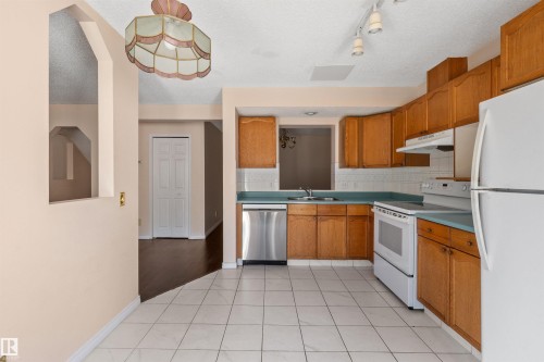 Kitchen featuring wood-finish cabinetry, white tile flooring, white appliances, and a stainless steel dishwasher - 5 20 Deerbourne Drive, St. Albert, AB 
