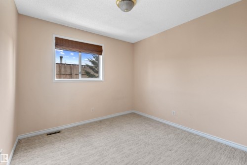 Bright interior room featuring a window with a woven wood shade, neutral wall tones, white trim, and textured carpeting - 5 20 Deerbourne Drive, St. Albert, AB 