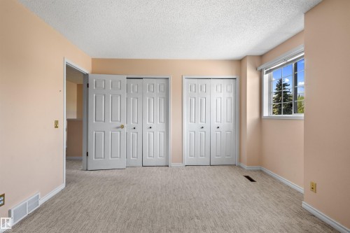 Room featuring textured carpet flooring, two bi-fold closet doors, and a window with white blinds - 5 20 Deerbourne Drive, St. Albert, AB 