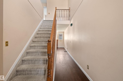 Foyer featuring a carpeted staircase with a wood-finish handrail, wood-finish flooring, and light-toned walls - 5 20 Deerbourne Drive, St. Albert, AB 
