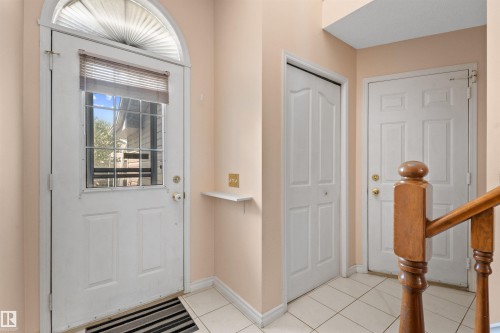 Entryway featuring a white paneled door with glass inserts and an arched transom window, ceramic tile flooring, a built-in shelf, and a light wood staircase banister - 5 20 Deerbourne Drive, St. Albert, AB 