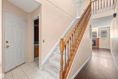 Entry foyer featuring white ceramic tile flooring and a view of the carpeted staircase with wood banister - 5 20 Deerbourne Drive, St. Albert, AB 