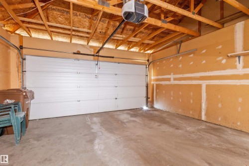 Spacious garage with a sectional overhead door, concrete flooring, exposed wooden ceiling trusses, and an automatic garage door opener - 5 20 Deerbourne Drive, St. Albert, AB 