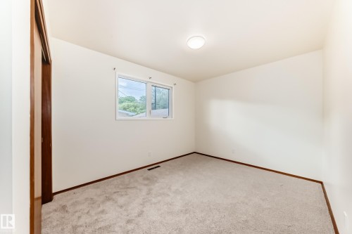 Bright room featuring neutral-toned carpet, white walls, wood trim, a double-pane window, and a flush-mount ceiling light - 12022 62 Street, Edmonton, AB 