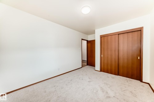 Carpeted room featuring light-colored walls and wood-finish sliding closet doors - 12022 62 Street, Edmonton, AB 