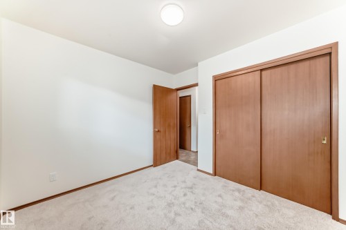 Carpeted interior space featuring a recessed ceiling light, wood-paneled doors, and sliding closet doors with matching wood-finish trim - 12022 62 Street, Edmonton, AB 