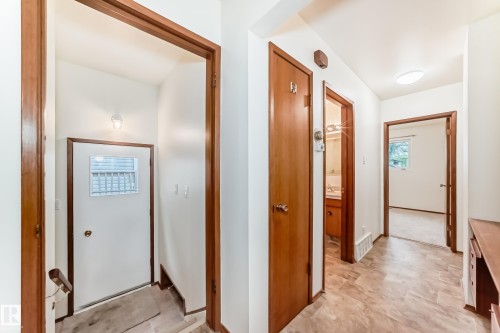 Foyer with white entry door featuring an opaque glass insert, illuminated by an overhead wall sconce, and wood-finish trim - 12022 62 Street, Edmonton, AB 