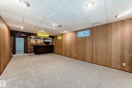 Spacious lower-level room featuring light wood-finish paneling and plush carpeting - 12022 62 Street, Edmonton, AB 