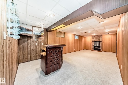 Finished lower level featuring a tufted built-in bar with wood-finish shelving, an exposed brick fireplace, recessed lighting, and wood-paneled walls - 12022 62 Street, Edmonton, AB 