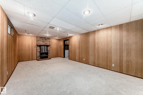 Finished basement with wood-panel walls, recessed lighting, and a brick fireplace featuring a black firebox - 12022 62 Street, Edmonton, AB 